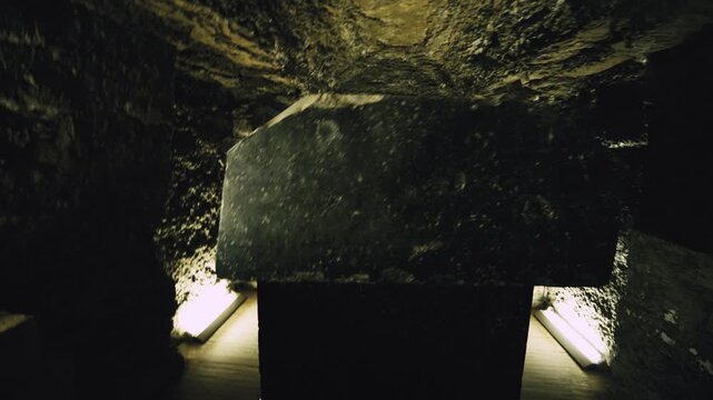 Eerie dimly lit underground burial corridor inside Serapeum of Saqqara near Cairo, Egypt, successive stone arches and warm golden spotlights revealing colossal sarcophagus.