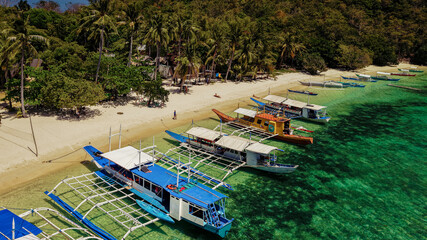 Aerial drone view of traditional Filipino outrigger boats anchored along the white sandy shoreline of Malcapuya Island in Coron, Palawan, Philippines. © akturer