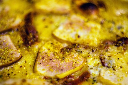 Zbliżenie makro na upieczoną pizzę z topionym serem, szynką i przyprawami. Apetyczna fotografia kulinarna o płytkiej głębi ostrości, idealna do menu lub bloga.