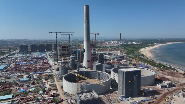 Coastal thermal power plant under construction with cooling towers and smokestacks visible