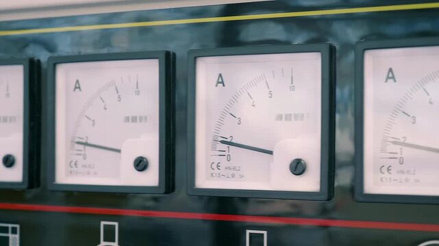 A long row of square pointer ammeters on a black, glossy industrial equipment. Closeup. Shot in motion