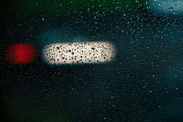 Raindrops on a window glass window at night with blurry car headlights and taillights bokeh on the background. © alan