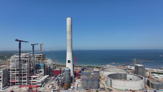Coastal nuclear power plant under construction featuring a towering cooling tower and seafront site