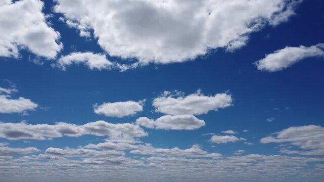 4K aerial drone view of scattered white cumulus clouds over a vast blue sky, cinematic high altitude flight, beautiful fair weather background for video projects, bright sunny day, atmospheric nature 