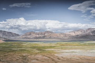 Landscape in the Tien Shan mountains in the Pamirs, mountains in the background and pastures with green fields in a valley with lakes and streams, a summer landscape for the background © Denis