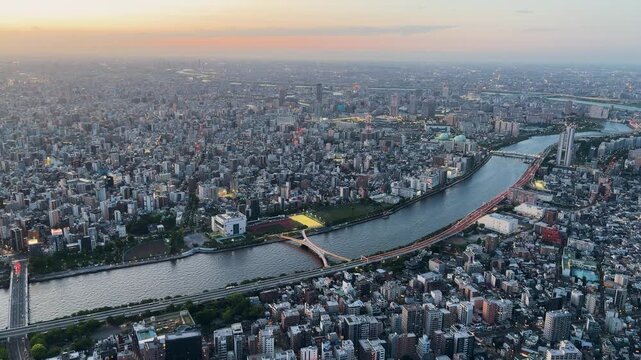 Aerial high-angle footage captures a panoramic evening view of Tokyo city from the Tokyo Skytree observation deck. The camera overlooks the winding Sumida River.