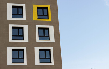Fototapeta premium Modern building facade featuring six rectangular windows, one highlighted in yellow, against a clear blue sky, showcasing contemporary architectural design elements