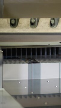 Industrial guillotine cutter slicing through stack of paper