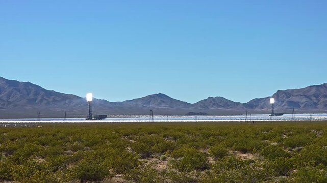 Twin Solar Power Towers Across Desert Valley, wide renewable energy video frame with heliostat mirrors and distant mountains