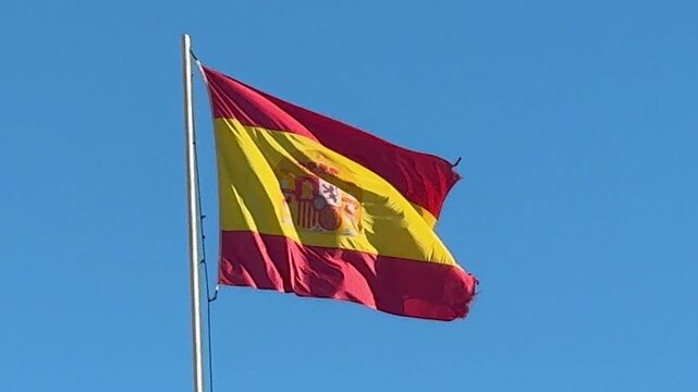 Flag of Spain Blowing in the Wind Against a Blue Sky