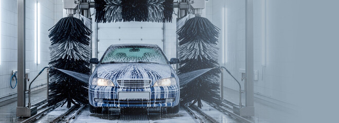 Fototapeta premium Car passing through automatic car wash tunnel. Vehicle covered in soap foam and water spray from brushes. Banner with copy space