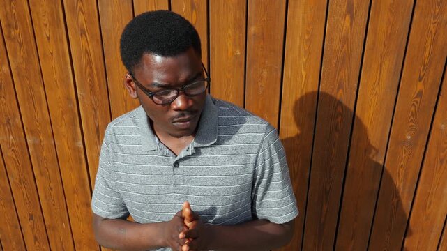 Man stands near wooden wall while looking down and thinking in a quiet outdoor setting