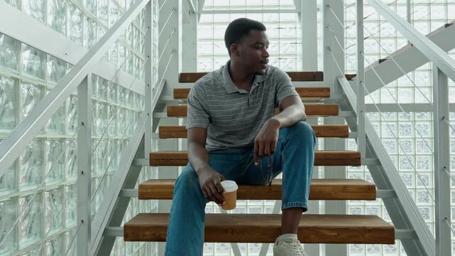 Man sitting on stairs in modern building with a drink in hand during afternoon