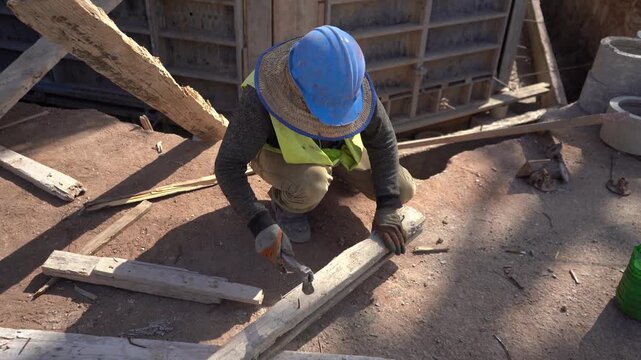 Construction worker in safety gear hammering wood at an active building site. Includes authentic ambient audio. Essential B-roll for manual labor, civil engineering, and infrastructure projects.