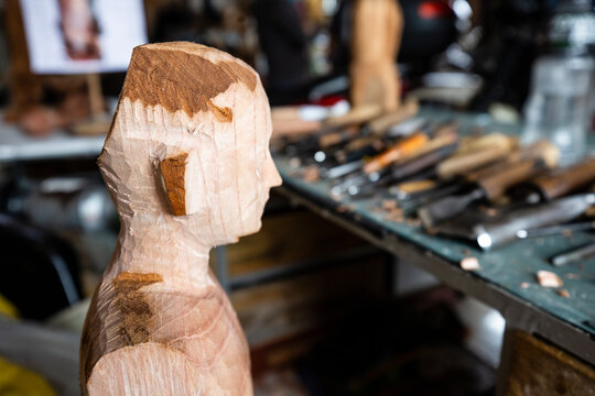 Hand carved wooden head profile close up with chisels and woodcarving tools background