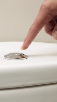 Male hand pushing a button to flush a close tool a bathroom toilet.