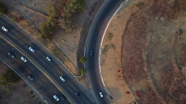 Top down aerial drone footage of curved highway exit with moving vehicles and dry urban landscape in Centro Sur Queretaro, Mexico during golden hour sunset