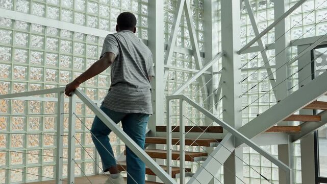 Man walks up modern steps inside a building with glass walls during the day
