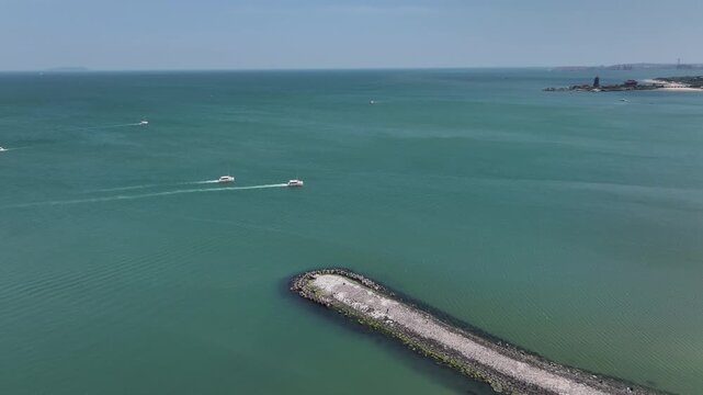Aerial view of a breakwater jetty with multiple speedboats navigating across the turquoise sea