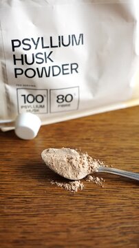 Heaped spoon of Psyllium husk powder on a wooden table next to the packaging.