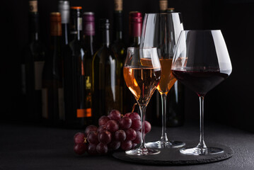 Fototapeta premium Three glasses of red, white and sparkling rose wine with bunch of grapes on dark slate background