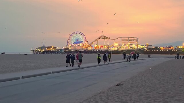 Santa Monica Pier Glowing At Sunset From Beach Path, scenic travel video frame with ocean lights, birds and evening sky