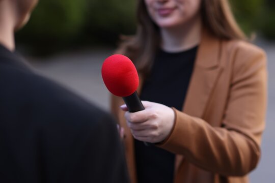 Professional journalist with microphone interviewing man outdoors, closeup