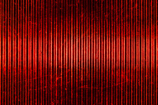 Macro shot of classic retro automobile red rear light lens. Textured ribbed glass surface with scratches creates a vibrant vintage abstract background