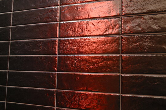 Dark rectangular tiles reflect vibrant red light, accentuating rough texture and grout lines.