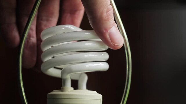 Closeup of a compact fluorescent light bulb mounted in a lamp frame against a dark wooden background.
