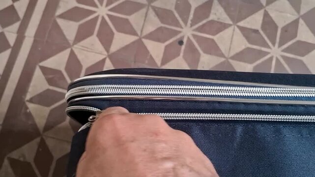 Hand pulling a metal zipper to securely close a dark blue fabric travel suitcase bag