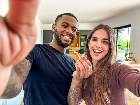 Happy couple celebrating new home with house keys while taking a joyful selfie in modern kitchen