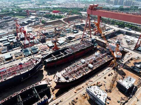Large shipyard scene with multiple vessel hulls under construction and heavy cranes in operation