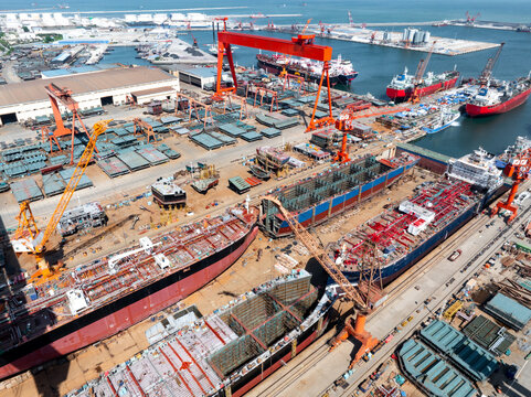 Large shipyard with active ship construction operations including hull assembly and crane handling
