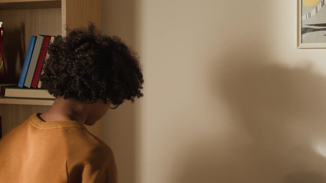 Rear medium close-up of young black schoolboy replacing handmade cartoon poster featuring superhero in cape with academic lesson timetable while preparing to begin new school year