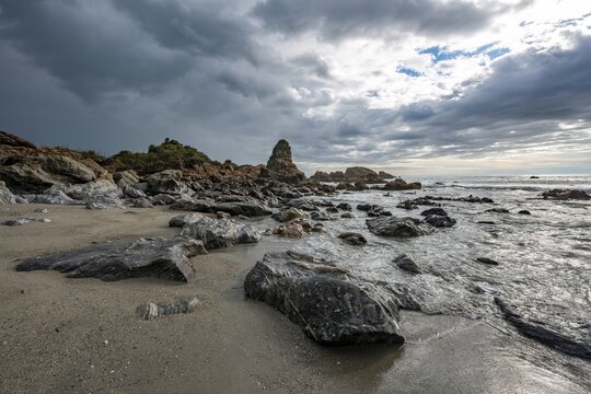 Rocky coast, rocks on the beach, dark rain clouds, long time exposure, West Coast, South Island, New Zealand