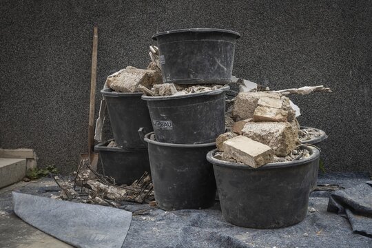 Shovel and large black round plastic containers filled with construction waste stand in front of a house wall, Stuttgart, Baden-W&uuml;rttemberg, Germany
