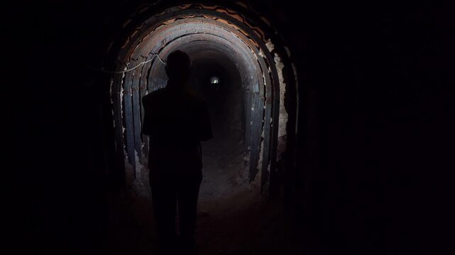 Cinematic silhouette of a person with a flashlight exploring a dark, abandoned mine shaft with rusty steel supports. Dramatic, moody B-roll ideal for thrillers, urbex, and mystery projects.