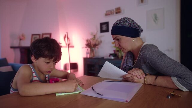 Mother undergoing chemotherapy homeschooling child at home table, headscarf parent guiding schoolwork with attentive focus, everyday learning moment showing care and resilience