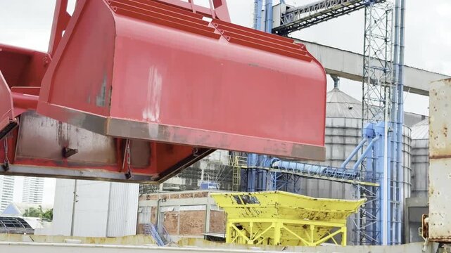 port terminal, ship with cargo hold fool of wheat moored. crane's grab lowered, closing, to take on wheat. grain leak from grab. operator wait for reduce scattering and bring cargo to port hopper. 