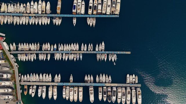 Aerial view of yachts moored in marina harbor along piers and docks at midday.