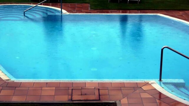 Swimming pool with blue water and tiled deck during a light rain shower in a resort setting