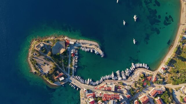 Aerial tracking shot of marina with yachts and boats mooring and sailing around island coastline of Datcha Turkey.