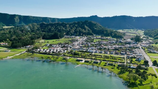 Aerial footage of white houses in Sete Cidades by lake shore surrounded by lush crater landscape