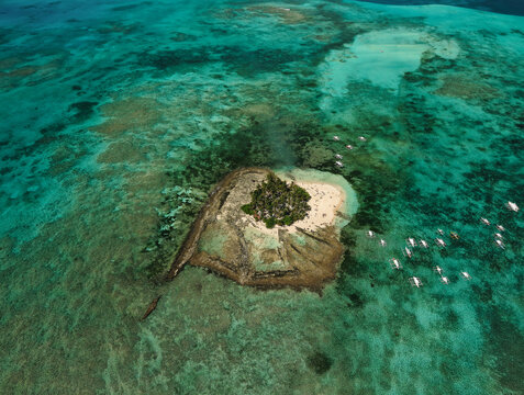 Aerial drone view of Guyam Island, a small tropical island surrounded by vibrant turquoise waters and coral reefs near Siargao, Philippines.