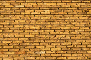 Fototapeta premium Textured background of an old yellow brick wall in warm evening sunlight. Full frame pattern of weathered sand-lime bricks with rough mortar joints.
