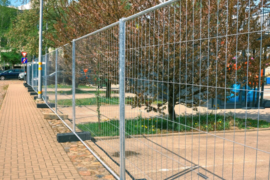 Temporary metal mesh fencing on a city sidewalk for event security. Mobile galvanized steel barrier panels installed for crowd control at an outdoor festival.