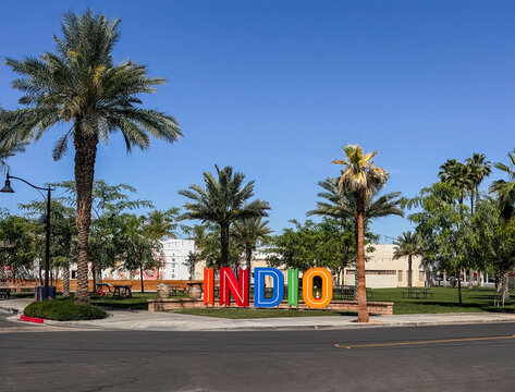 Indio, California, USA - April 15, 2026: Colorful name sign along road on side of green park with plenty of palm and other trees under blue sky