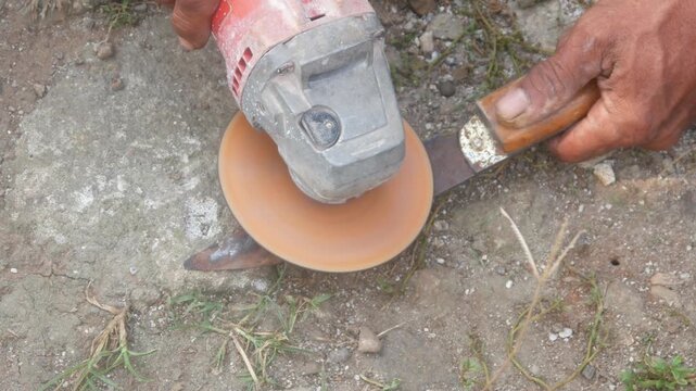 Workers are sharpening or sharpening traditional knife blades using a hand grinder in an outdoor area.