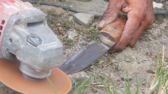 Workers are sharpening or sharpening traditional knife blades using a hand grinder in an outdoor area.